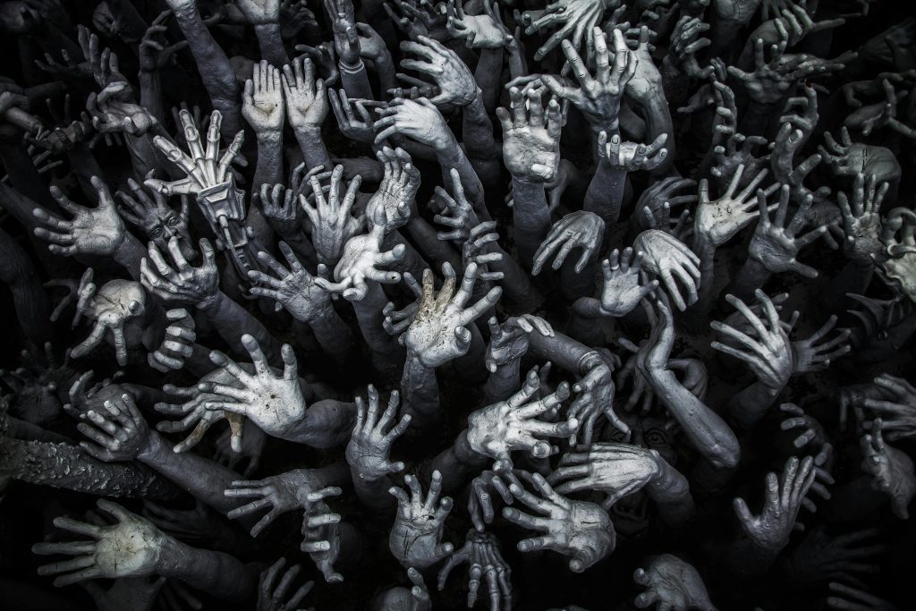 A haunting display of numerous grey hands reaching upward at Wat Rong Khun, Thailand.