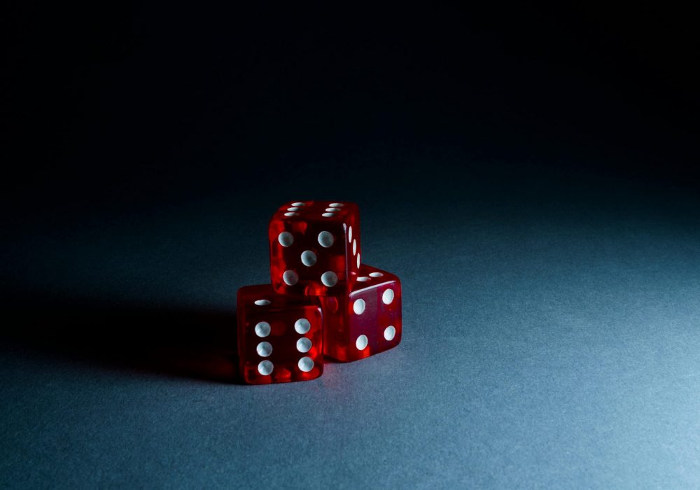 Projects Three red transparent dice stacked on a dark surface, highlighting their reflective surfaces and dots.